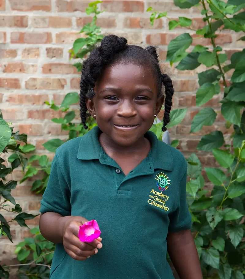 A young girl holds a pink flower, her green polo shirt reads "Academy of Global Citizenship"