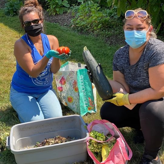 Two adults wearing masks show off freshly picked produce from their containers