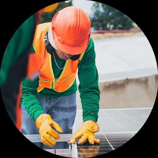 A solar technician works on a solar panel while wearing bright orange safety gear.