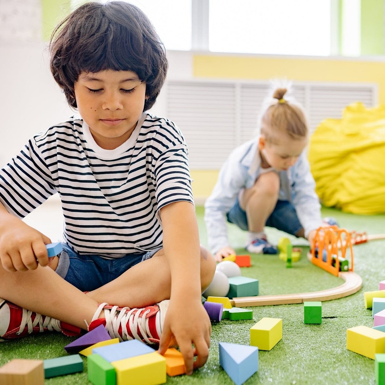 Children play with blocks and trains in a classroom.