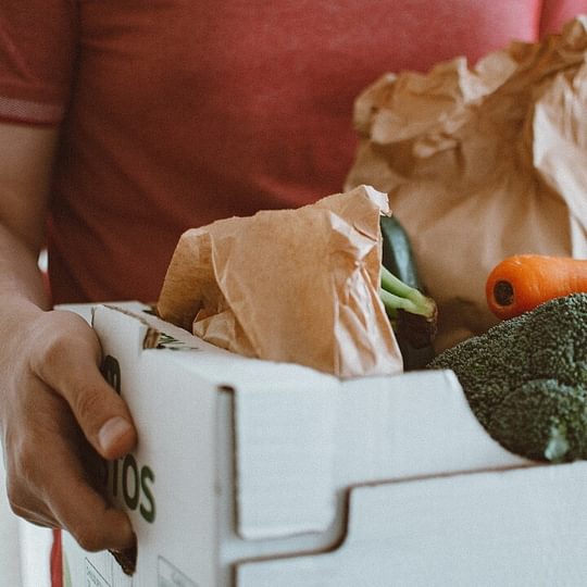 A closeup photo of a produce box, filled with bagged veggies such as carrots and broccoli