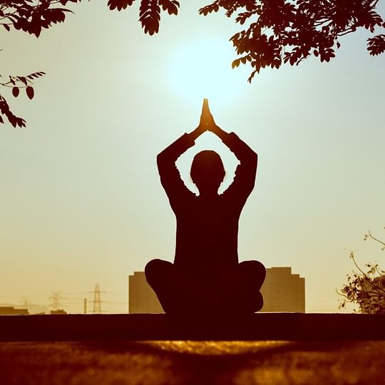 Silhouette of a yoga pose against sunset in the city.